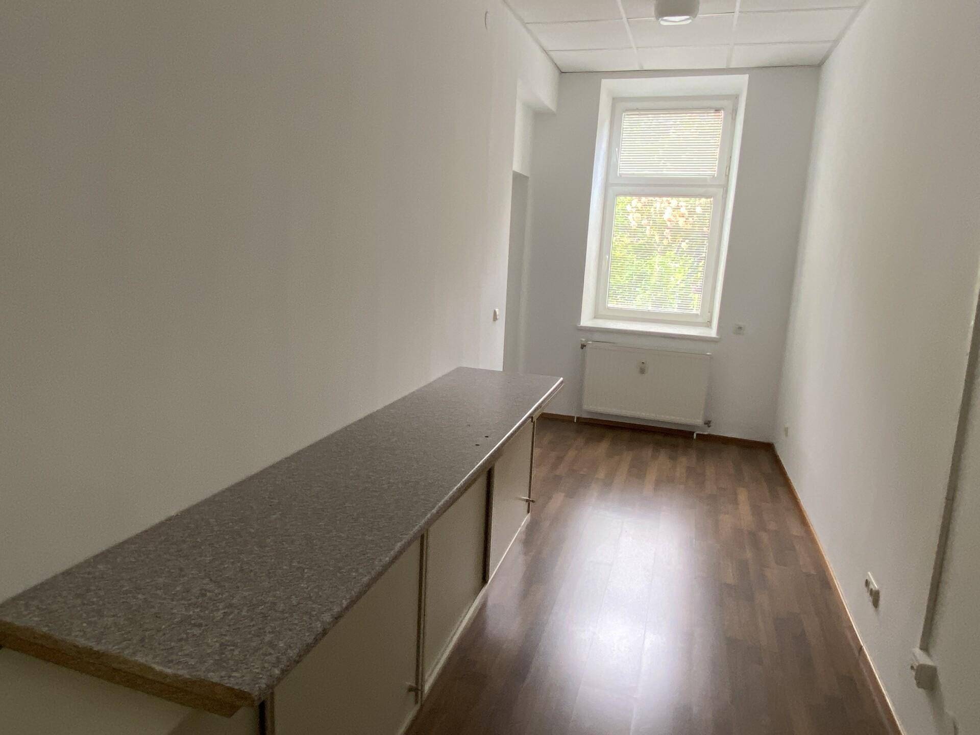 Langer, schmaler Büroraum mit einem Fenster, Heizkörper und einer langen Ablagefläche an der Wand.