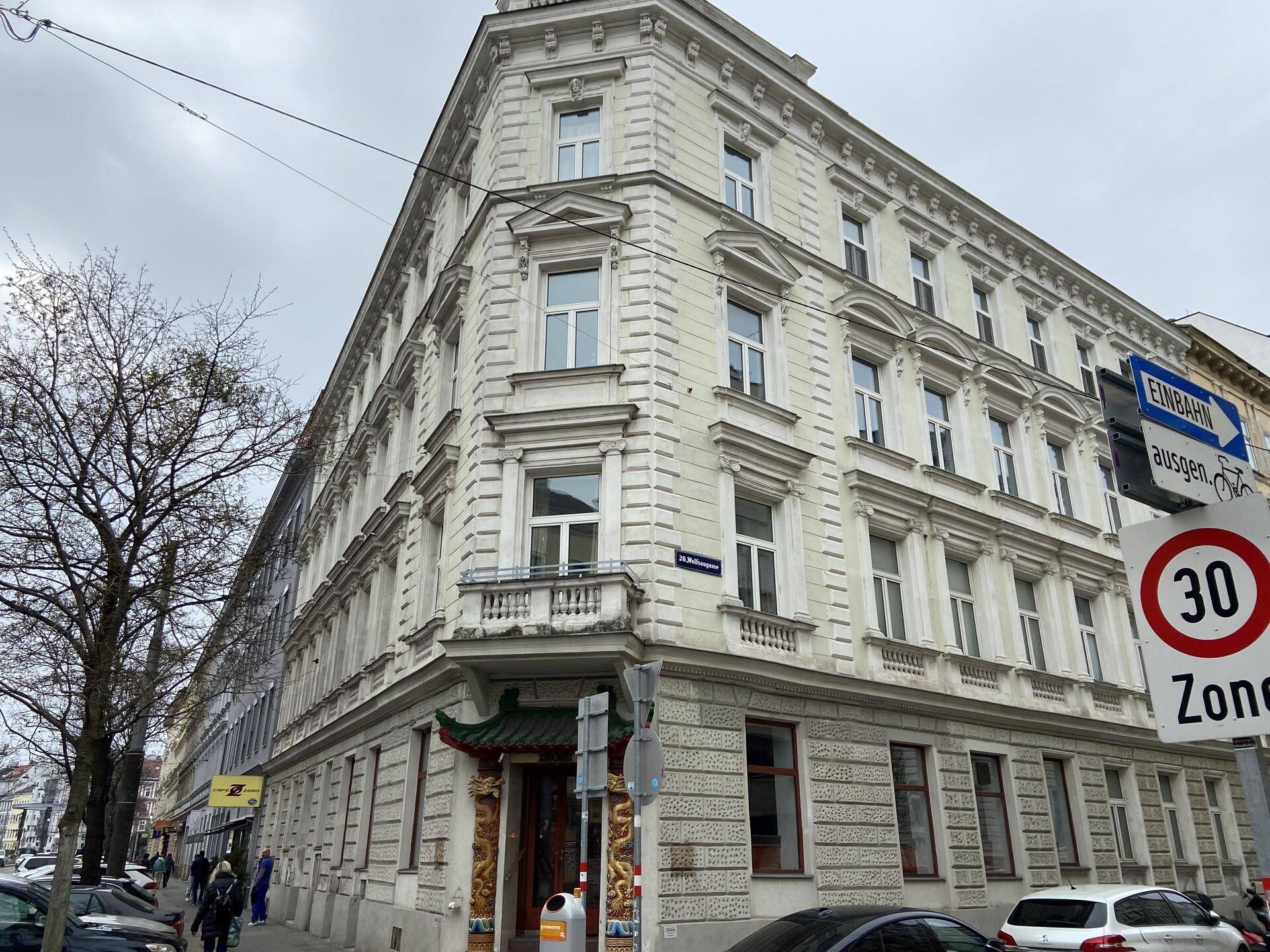 Historisches Eckgebäude mit klassischer Architektur, vielen Fenstern und belebter Straßenszene.