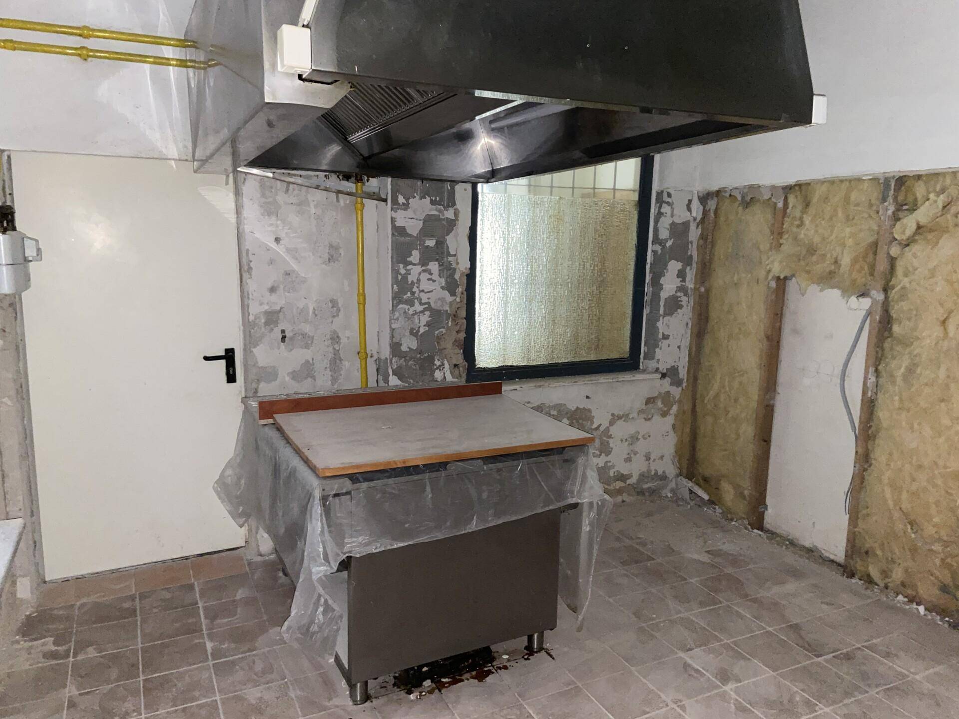 Gewerbliche Küche in Renovierung mit großer Dunstabzugshaube, Arbeitstisch und freigelegten Wänden.