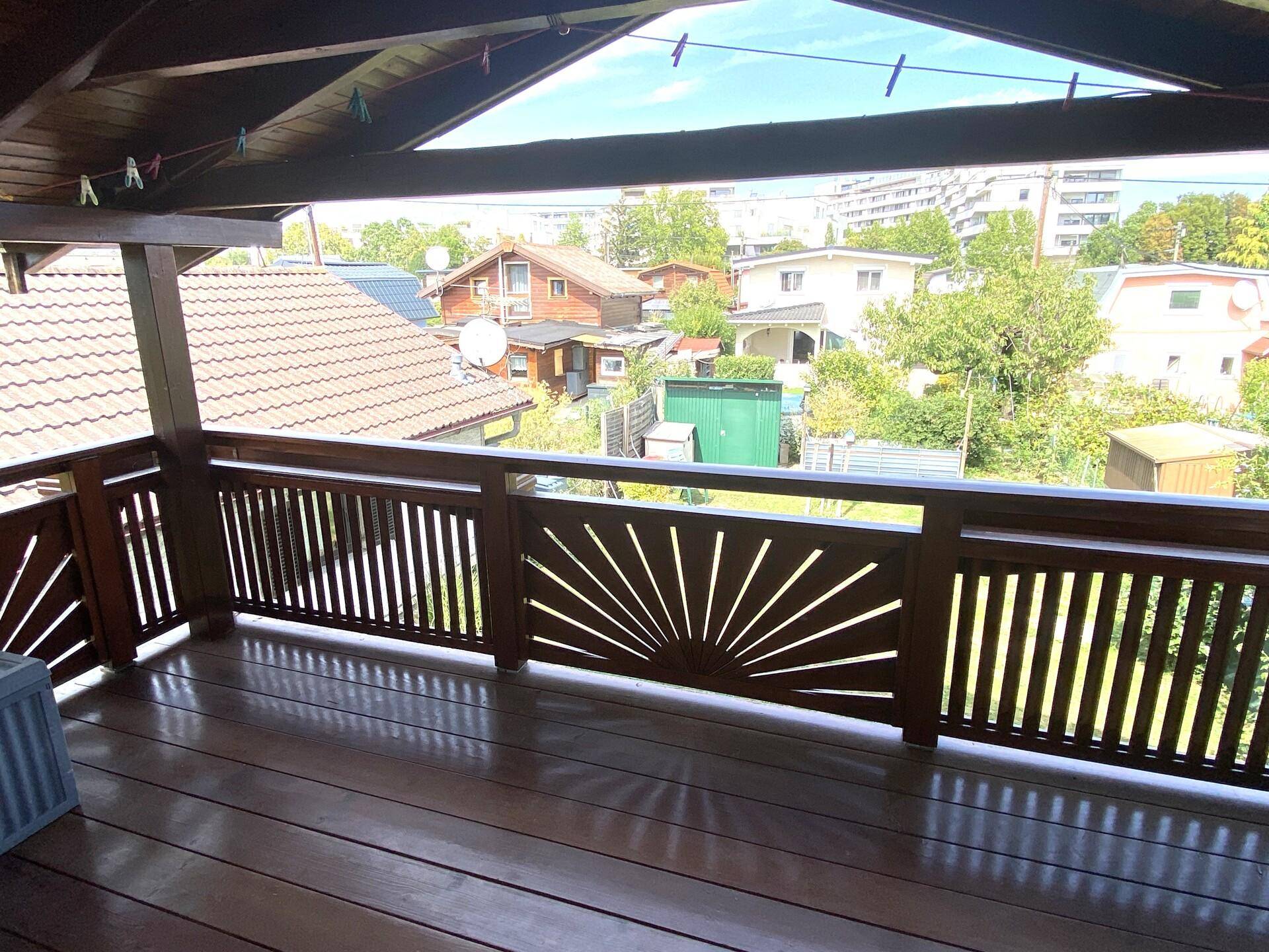 Geräumiger überdachter Balkon mit Holzboden und dekorativem Geländer, bietet Weitblick.