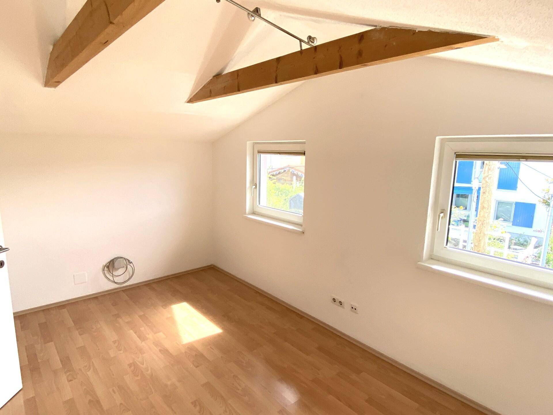 Helles Schlafzimmer im Dachgeschoss mit Holzbalken, Schrägdach und Laminatboden.