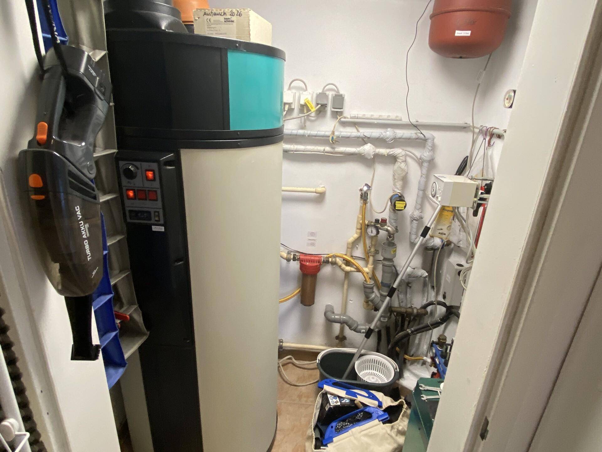 Technikraum mit Heizungsanlage, Rohren und Stauraum für Haushaltsgeräte.