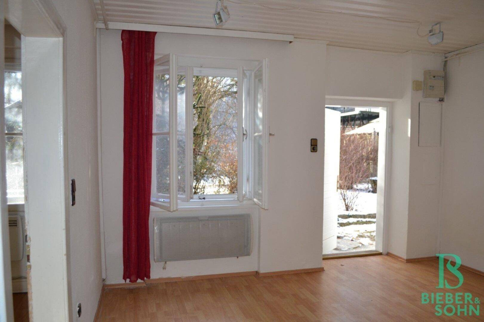 Ein heller Raum mit Laminatboden und einem Fenster, das einen Blick auf die verschneite Landschaft bietet.