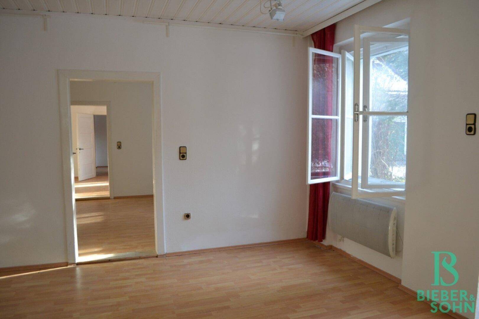 Ein heller Raum mit Laminatboden, weißen Wänden und einem Fenster, das Tageslicht hereinlässt.