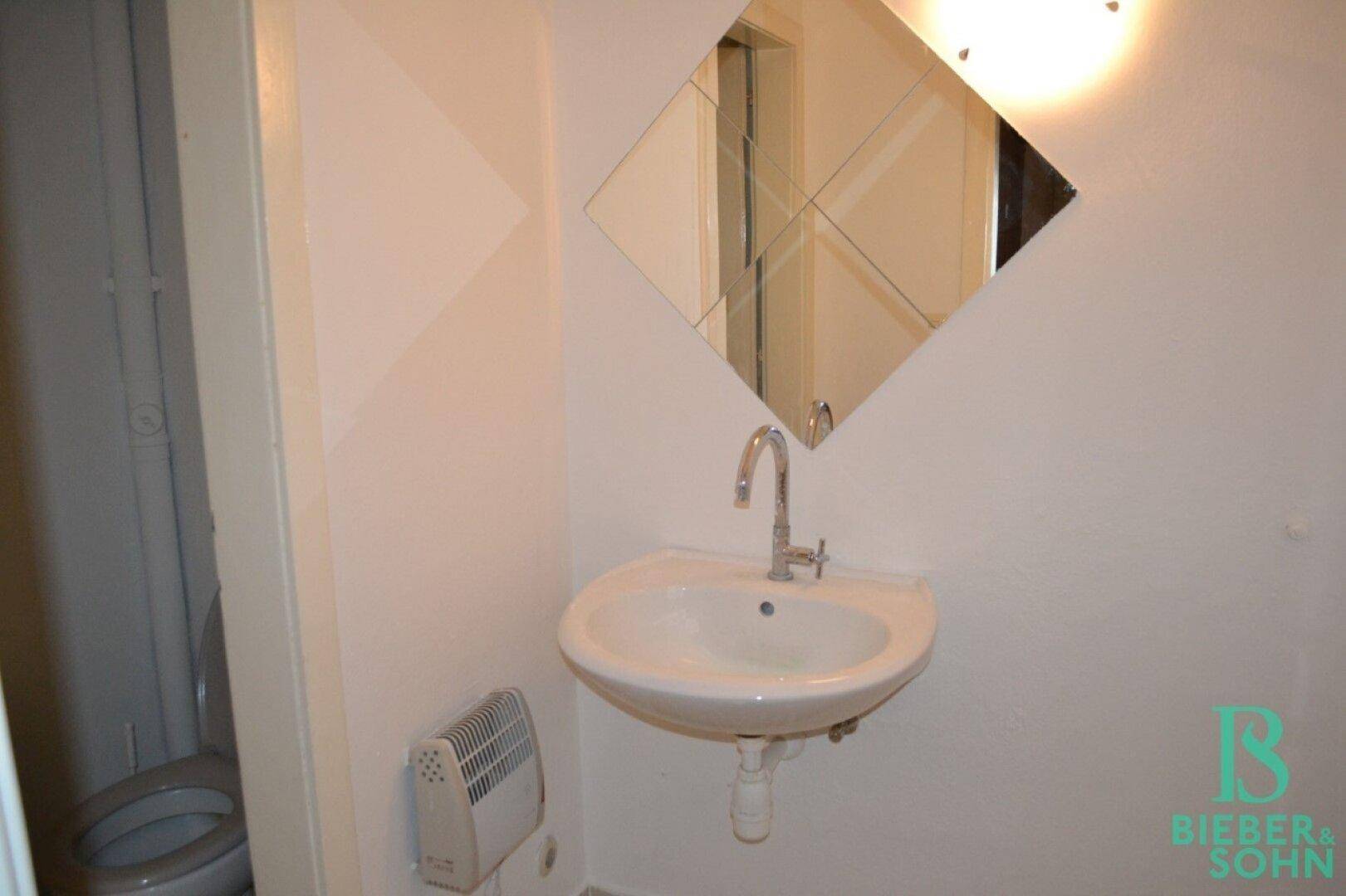Ein kleines Badezimmer mit Waschbecken, Spiegel und einer Heizung an der Wand.
