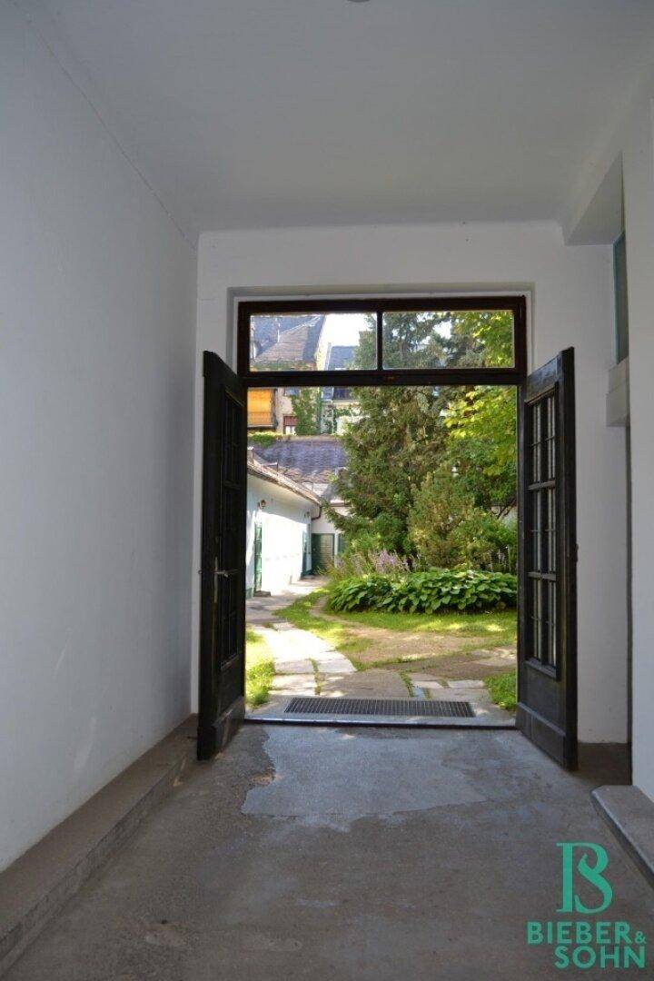 Ein Eingangsbereich mit geöffneten Türen, die den Blick auf einen grünen Gartenweg freigeben.