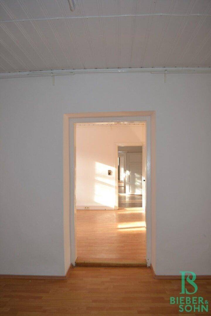 Ein heller Raum mit Laminatboden und einem offenen Durchgang, der zu weiteren Zimmern führt.