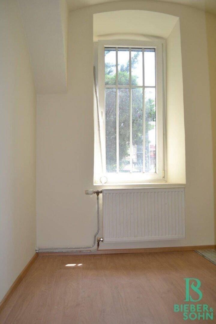 Detailansicht eines hohen Fensters mit Sprossen und einem Heizkörper darunter in einem hellen Raum.