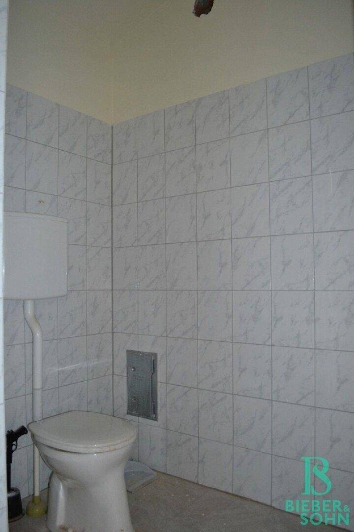 Kleiner Toilettenraum mit weißen Fliesen an den Wänden und einem einfachen WC.