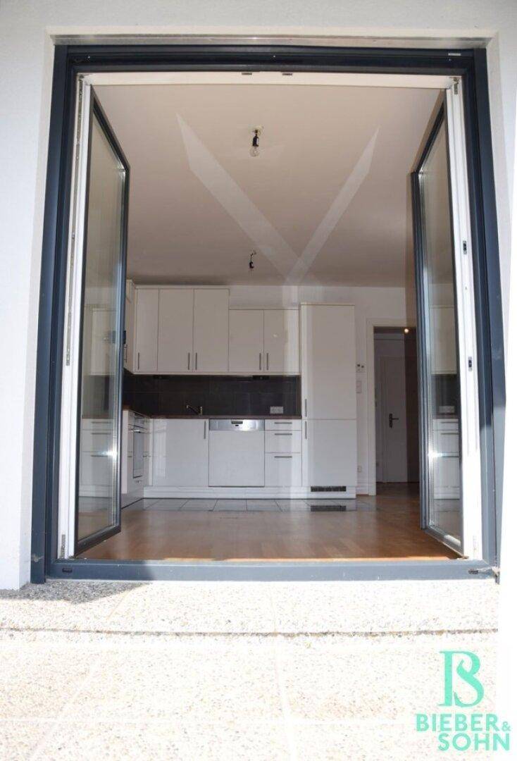Blick von außen in eine moderne Küche mit weißen Schränken und integrierten Geräten.
