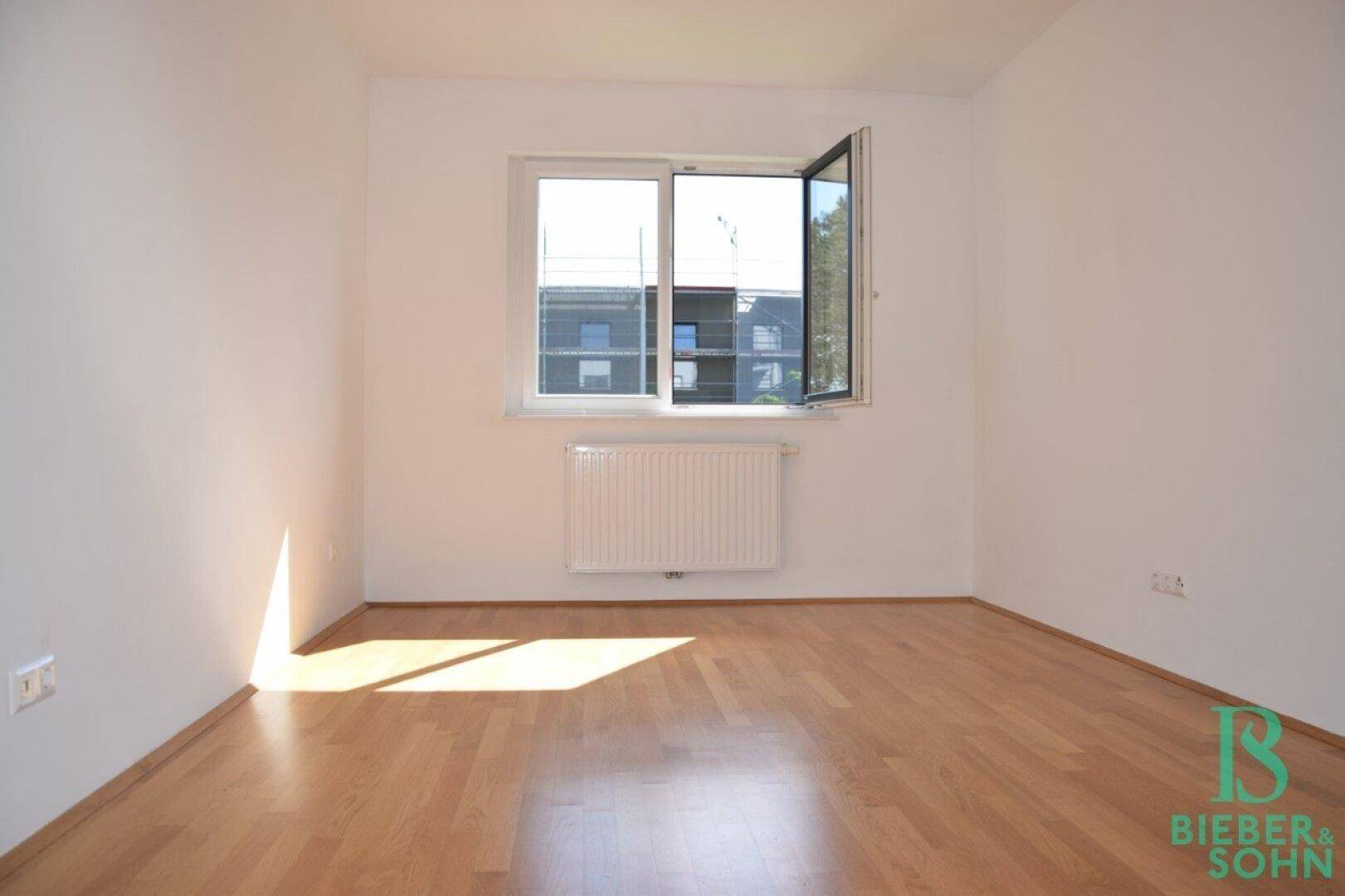 Geräumiger, heller Raum mit Parkettboden, weiß gestrichenen Wänden und einem großen Fenster.