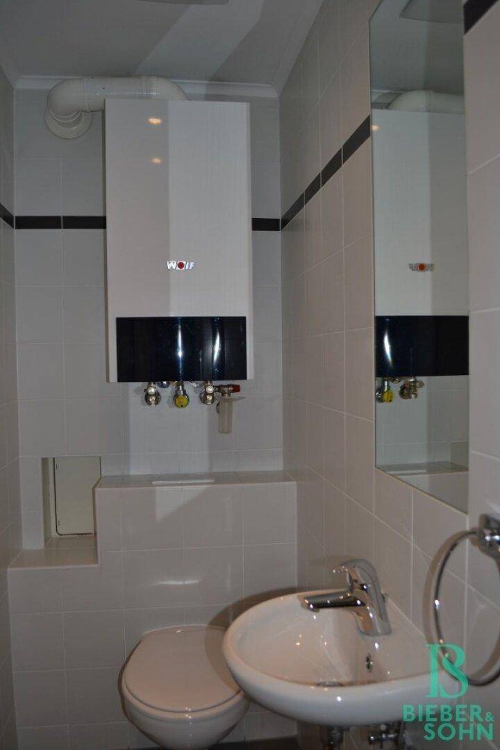 Kleines Badezimmer mit WC, Waschbecken und wandmontiertem Warmwasserbereiter, gefliest in Weiß und Schwarz.