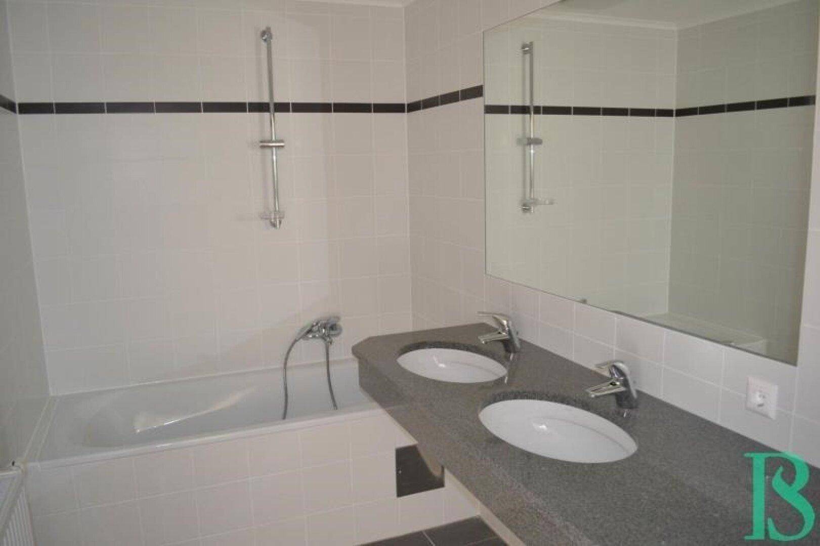 Modernes Badezimmer mit Badewanne, Doppelwaschbecken und großem Spiegel, gefliest in Weiß und Schwarz.