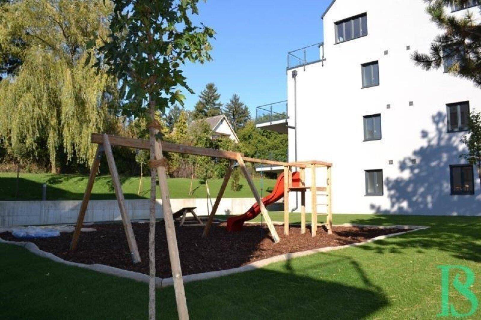 Kinderspielplatz mit Schaukel und Rutsche auf einer Grünfläche neben dem Wohngebäude.