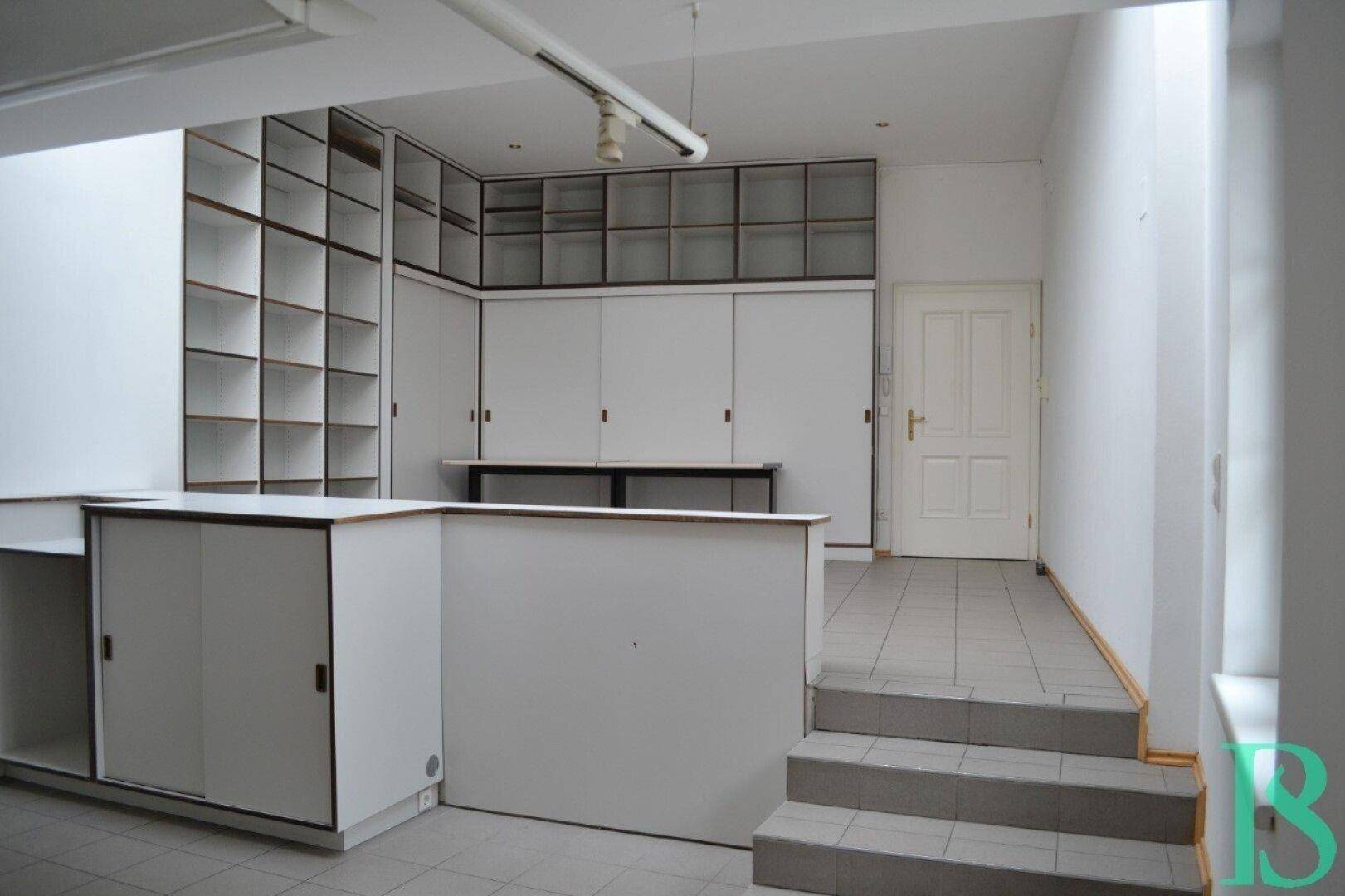 Gewerbefläche mit Einbauregalen, Theke und gefliestem Boden, ideal für Laden oder Büro.