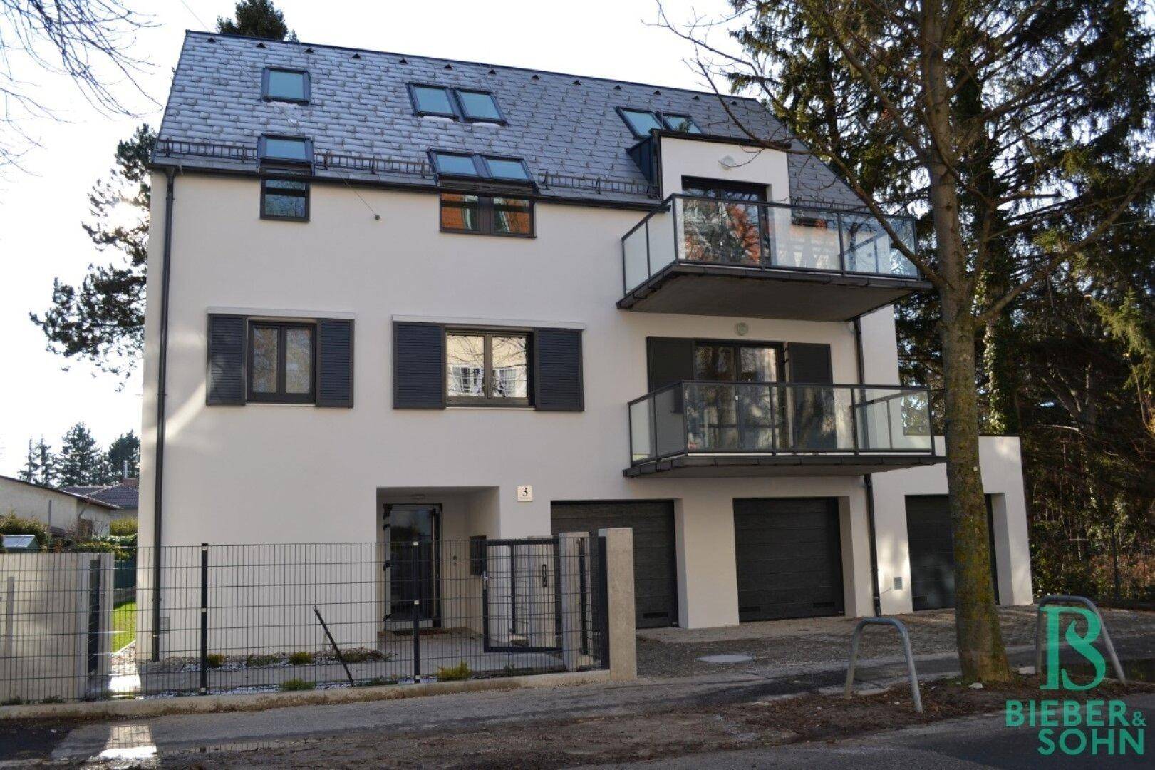 Modernes Mehrfamilienhaus mit weißer Fassade, dunklen Fensterläden und Glasbalkonen.