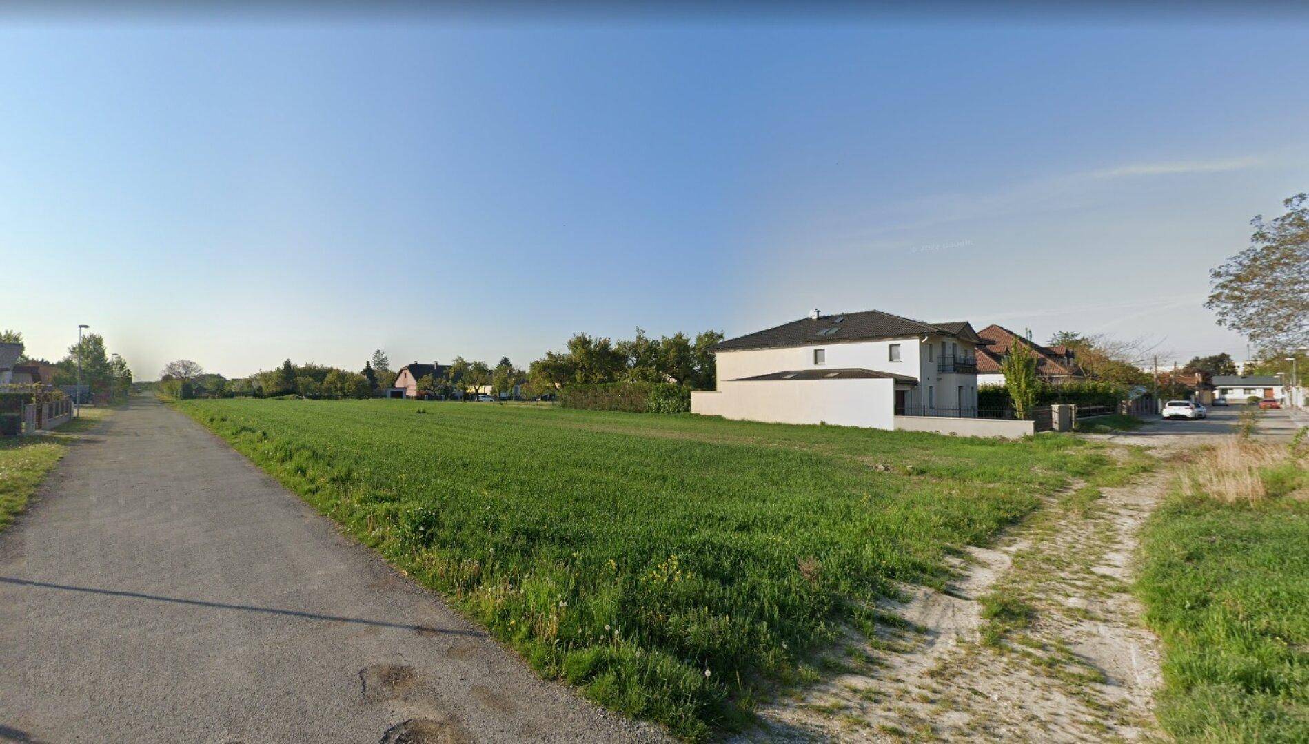 Offenes Feld mit einem Feldweg im Vordergrund und Wohngebäuden am Horizont.