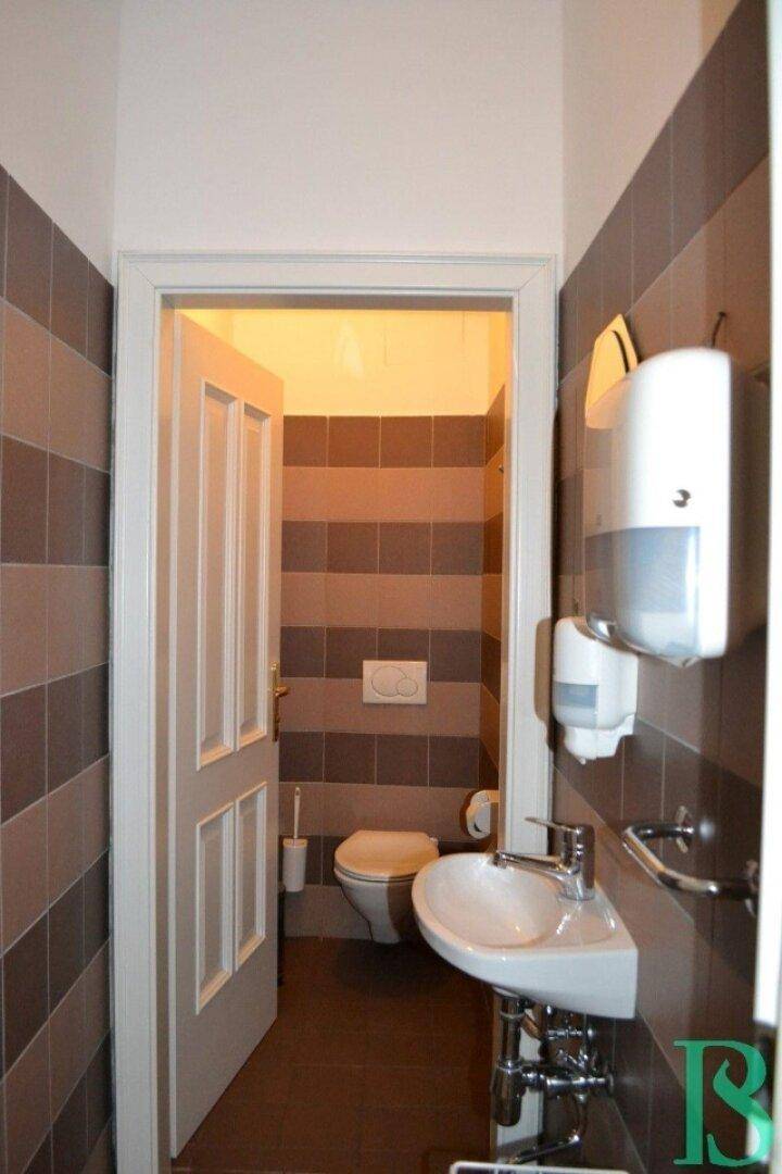 Kleine Toilette mit gestreiften Fliesen, wandhängendem WC und Waschbecken mit Seifenspender.