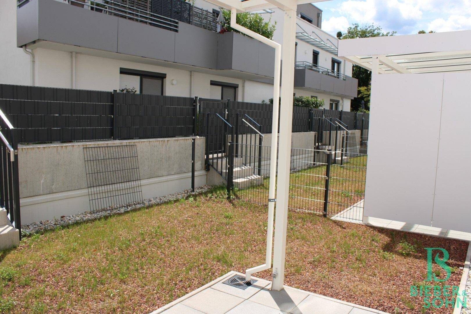 Kleiner Gartenbereich mit Terrasse und Zaun, angrenzend an moderne Wohngebäude.
