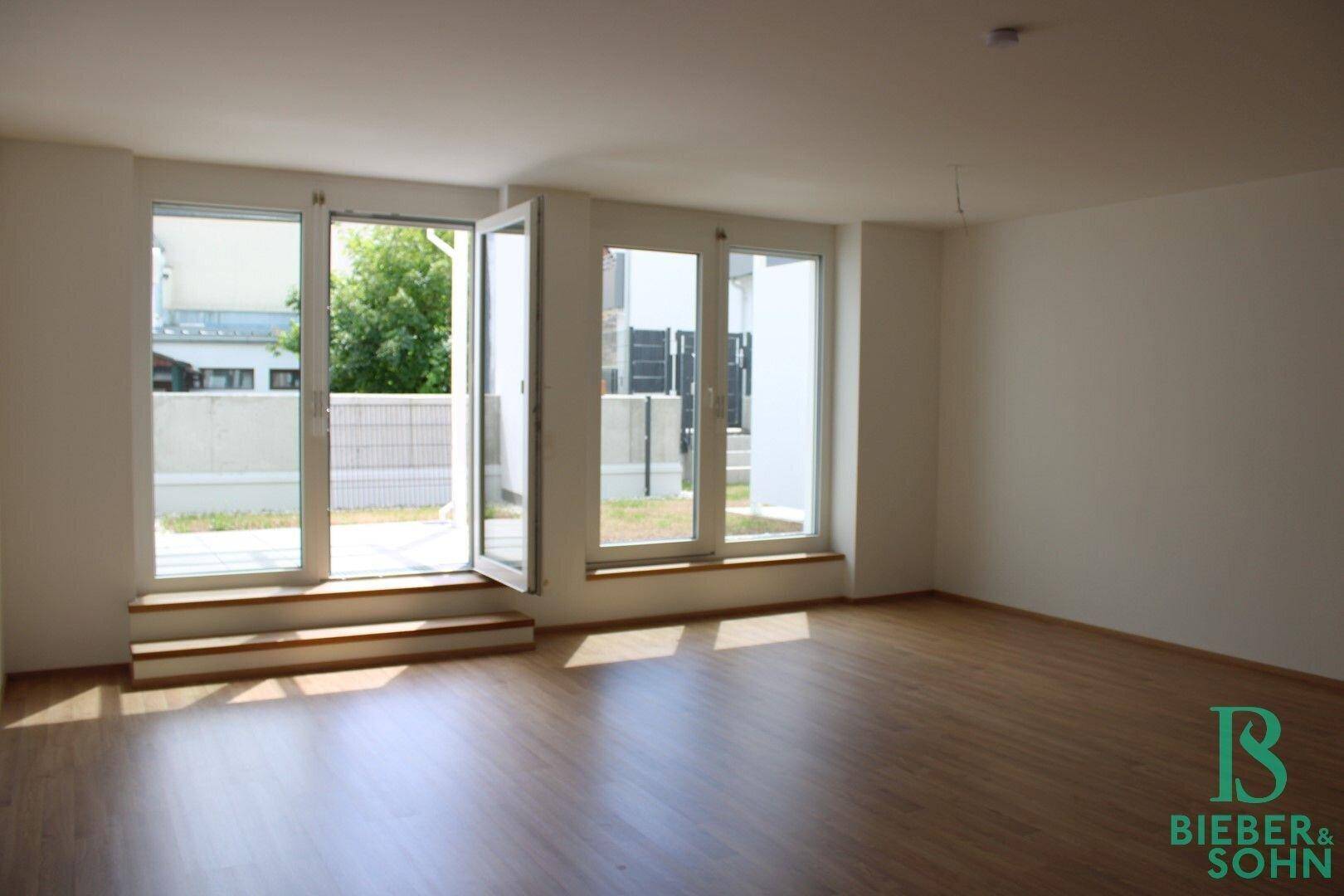 Helles Wohnzimmer mit Holzboden und großen Fenstern, die Zugang zur Terrasse bieten.