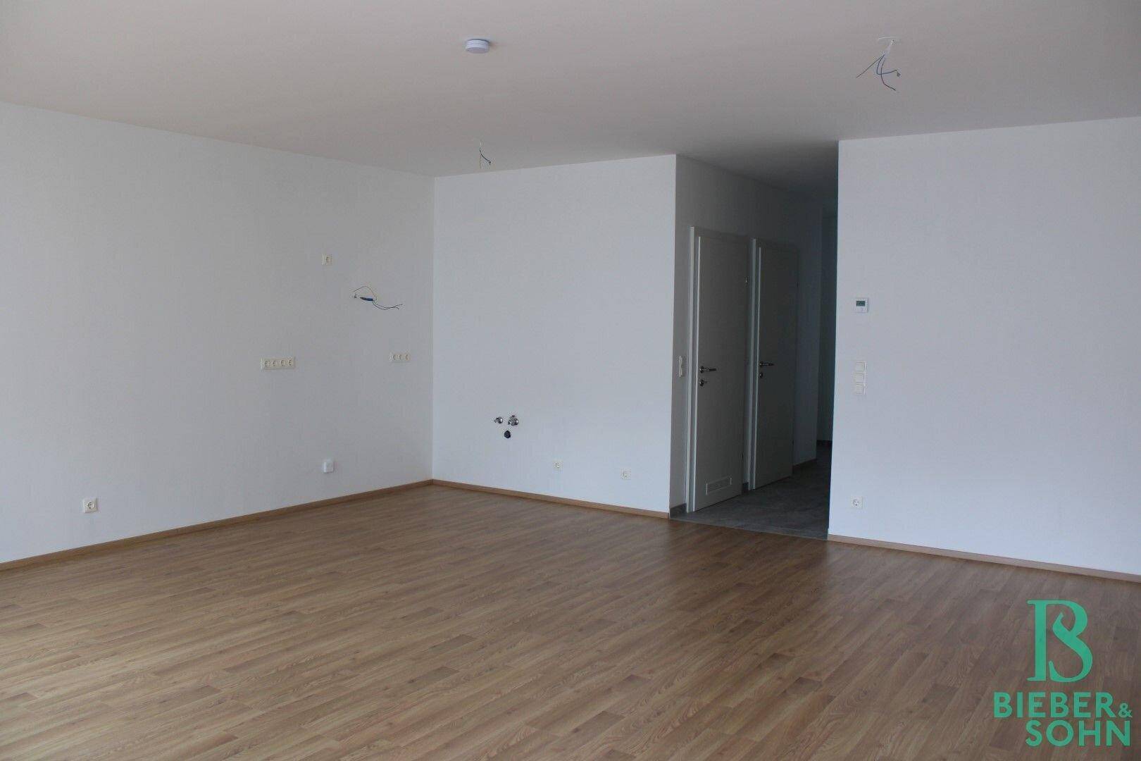 Geräumiges Wohnzimmer mit hellem Laminatboden und weißen Wänden, bereit für individuelle Gestaltung.