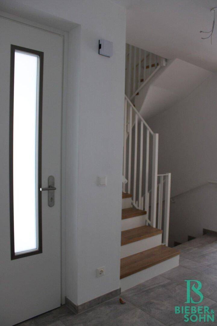 Eingangsbereich mit Holztreppe und weißem Geländer, führt in die oberen Etagen.