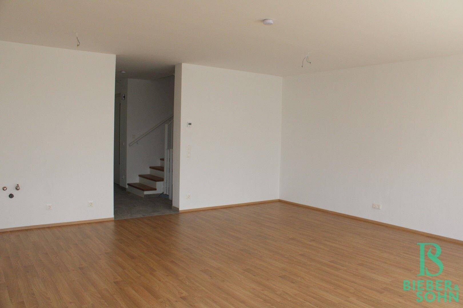 Helles Wohnzimmer mit Laminatboden und Zugang zur Treppe, ideal für offenes Wohnen.