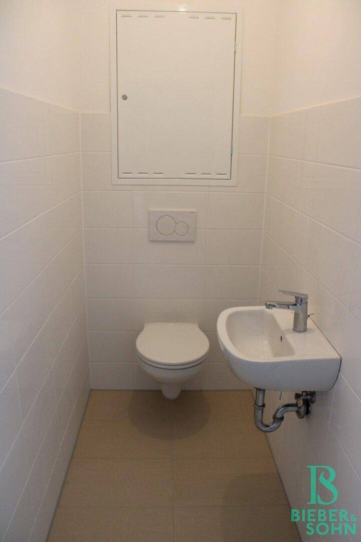 Modernes Gäste-WC mit Wand-WC und kleinem Waschbecken, hell gefliest.