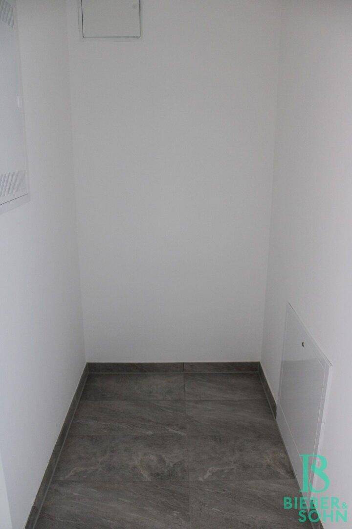 Leerer Raum mit dunklem Fliesenboden und weißen Wänden, ideal als Abstellraum.