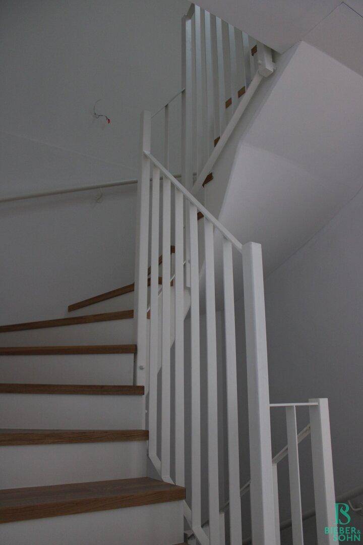 Wendeltreppe mit Holzstufen und weißem Geländer, verbindet die Stockwerke.