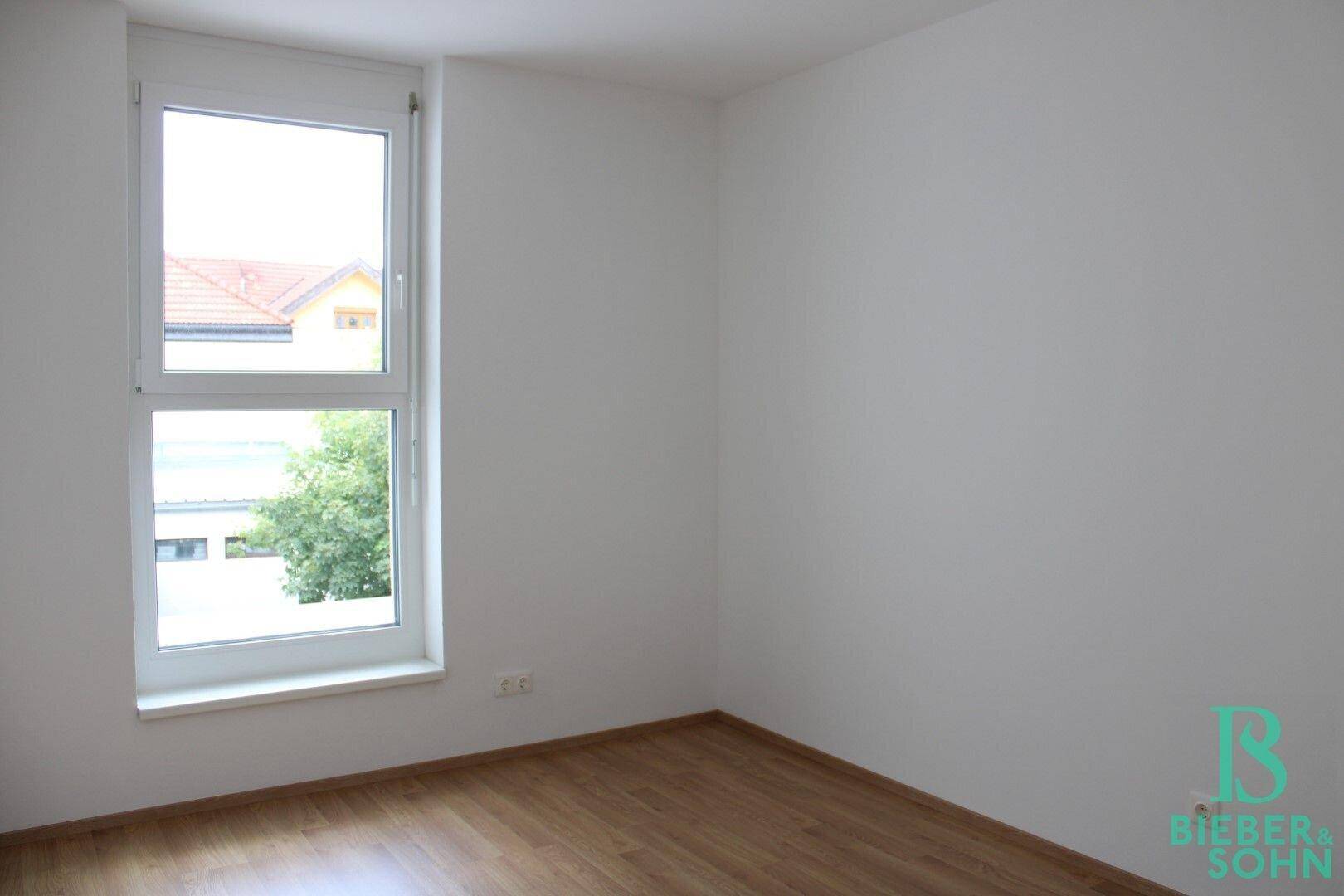 Schlafzimmer mit Laminatboden und großem Fenster, das viel Tageslicht hereinlässt.
