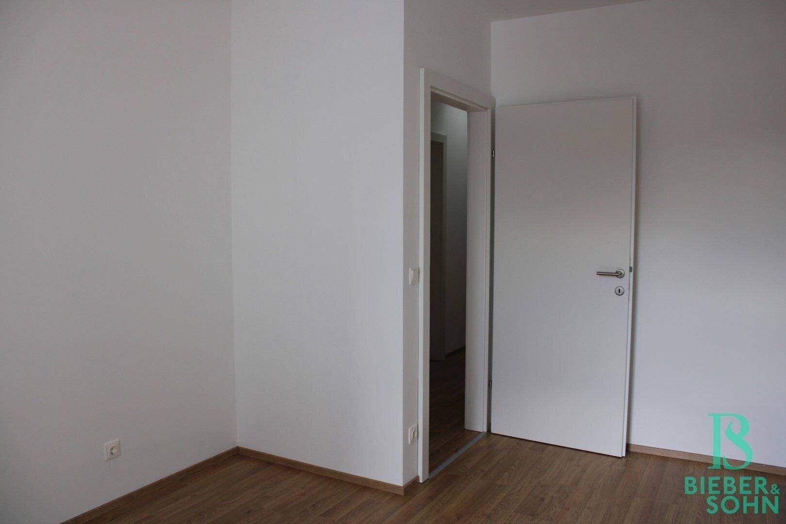 Schlafzimmer mit Laminatboden und weißer Tür, bereit für die Einrichtung.