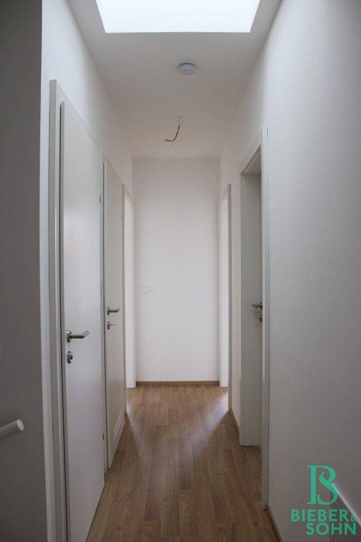 Heller Flur mit Holzboden und mehreren Türen, beleuchtet durch ein Oberlicht.