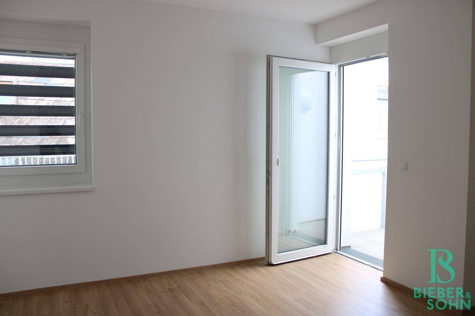 Helles Zimmer mit Holzboden und Zugang zu einem Balkon, bietet frische Luft.