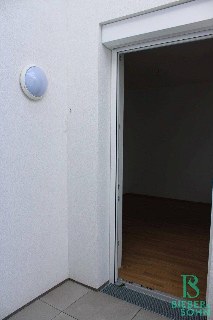 Zugang zum Balkon von einem Innenraum, mit Außenleuchte und Fliesenboden.