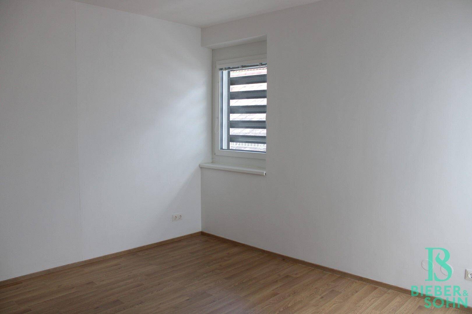 Schlafzimmer mit Laminatboden und Fenster mit Jalousien, bietet Privatsphäre und Lichtregulierung.