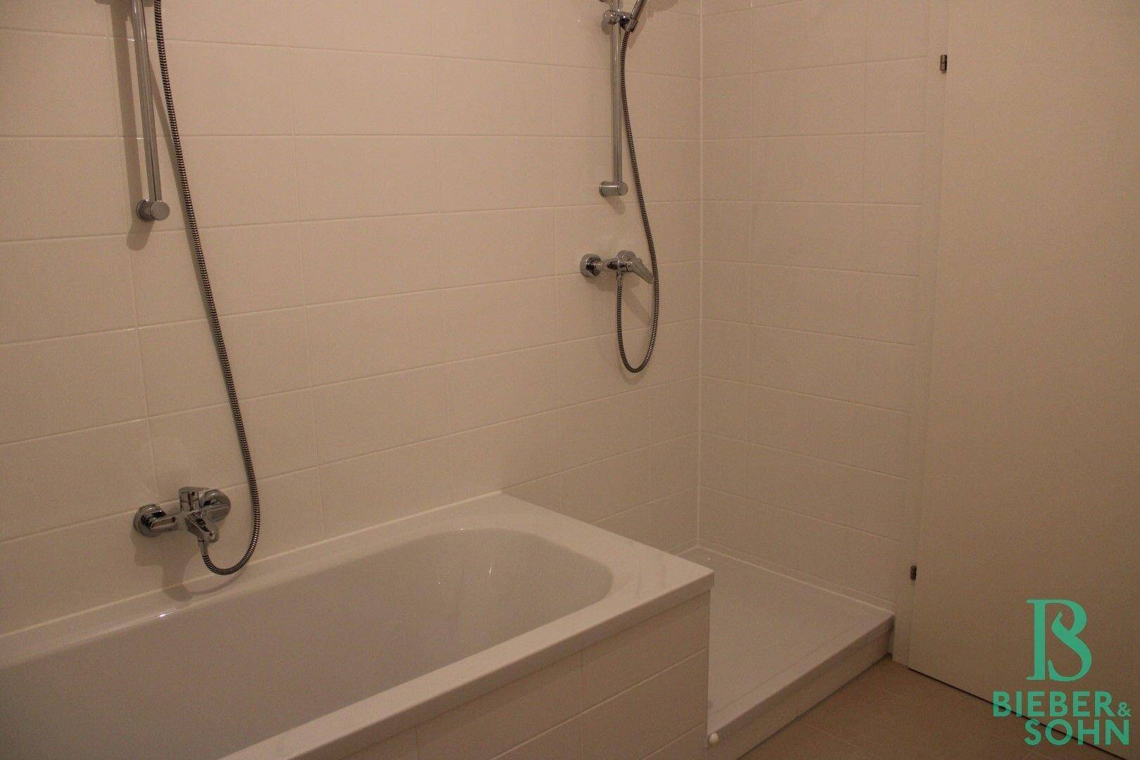 Modernes Badezimmer mit Badewanne und Duschbereich, hell gefliest.