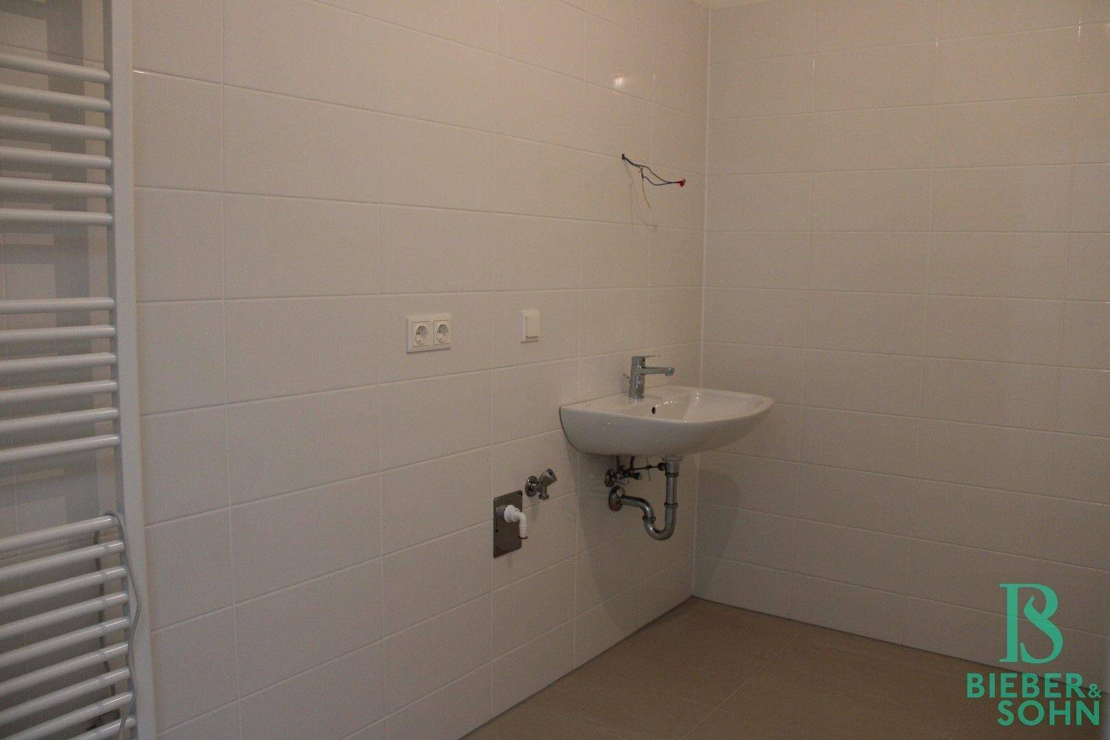 Modernes Badezimmer mit weiß gefliesten Wänden und Einzelwaschbecken, inklusive Handtuchheizkörper.