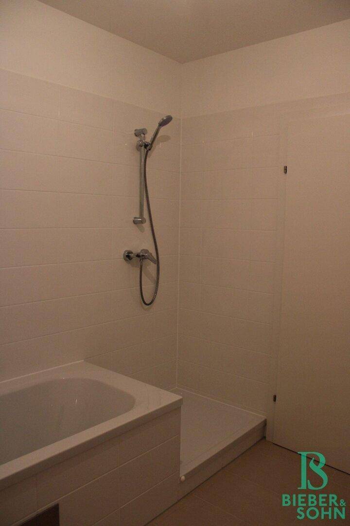 Helles Badezimmer mit Badewanne und Duschbereich, ausgestattet mit modernen Armaturen.