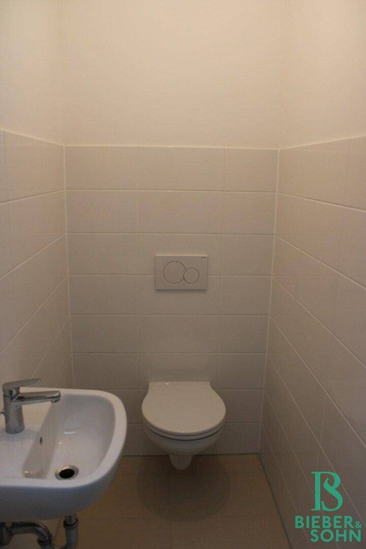 Kleines Gäste-WC mit Wand-WC und Waschbecken, in neutralen Farben gehalten.