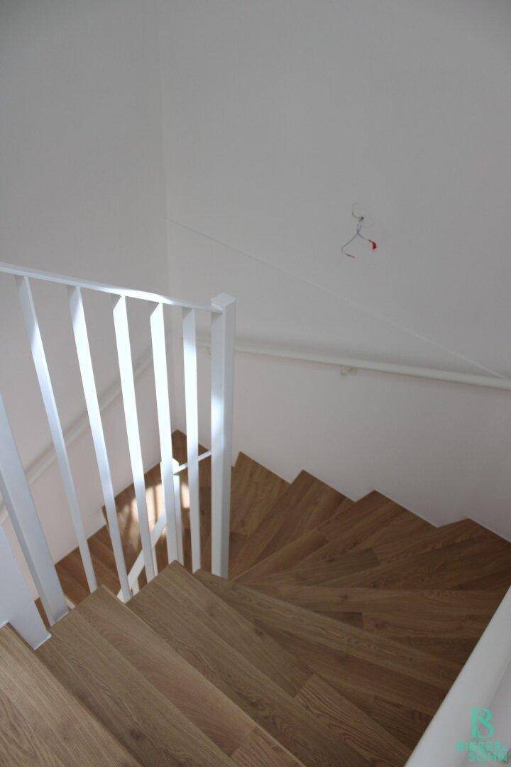 Treppenhaus mit Holzstufen und weißem Geländer, das die oberen Etagen verbindet.