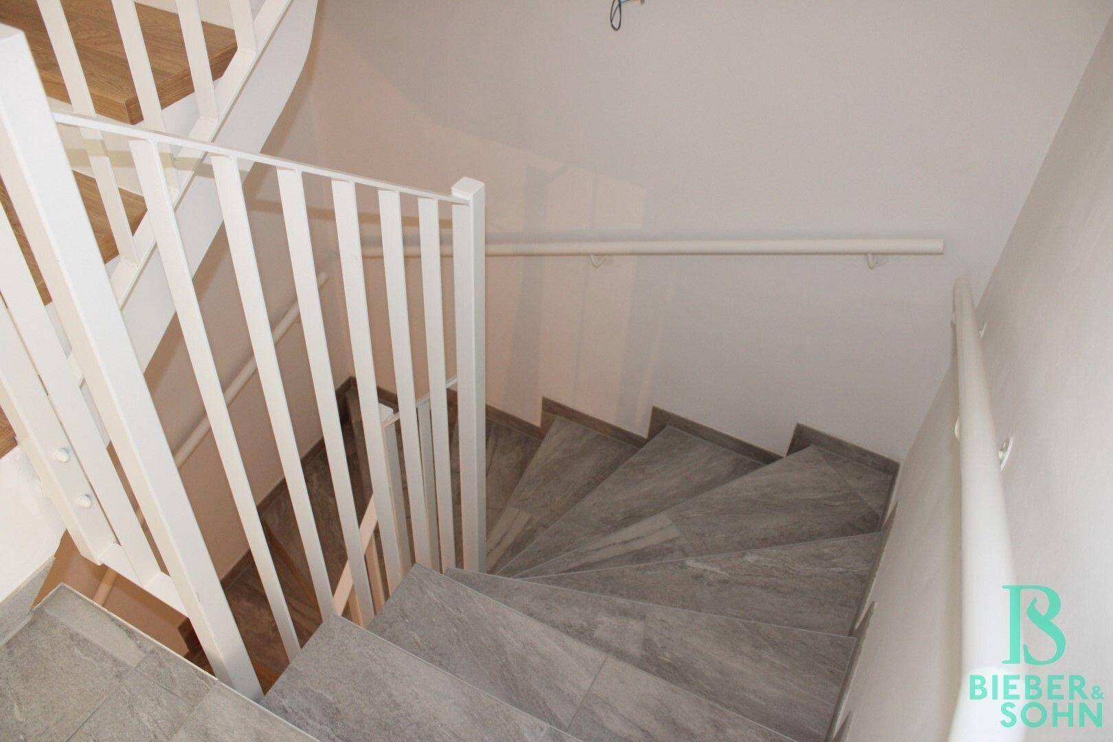 Treppenhaus mit gefliesten Stufen und weißem Geländer, führt in die unteren Etagen.