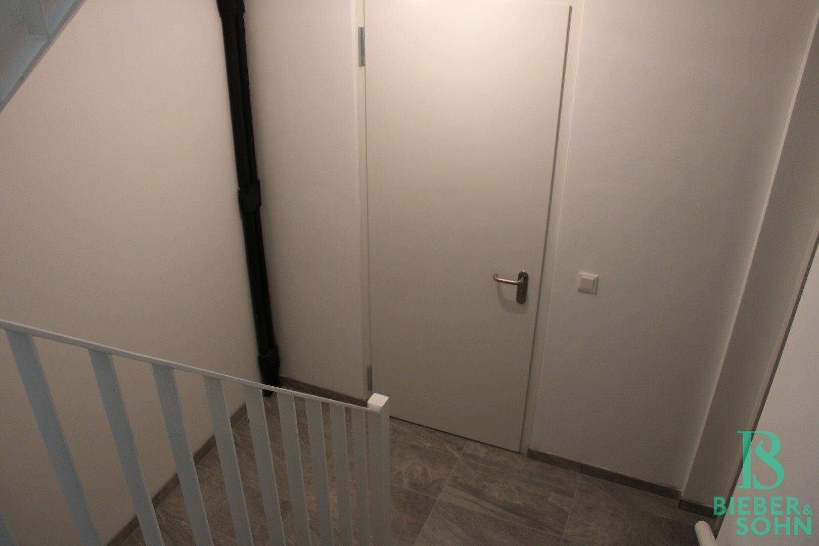 Moderner Treppenbereich mit weißen Wänden, grauen Fliesen und einer schlichten Tür.