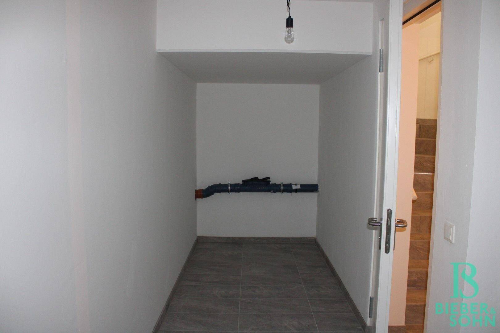 Kleiner Abstellraum mit Fliesenboden und sichtbaren Rohren, ideal für Lagerzwecke.