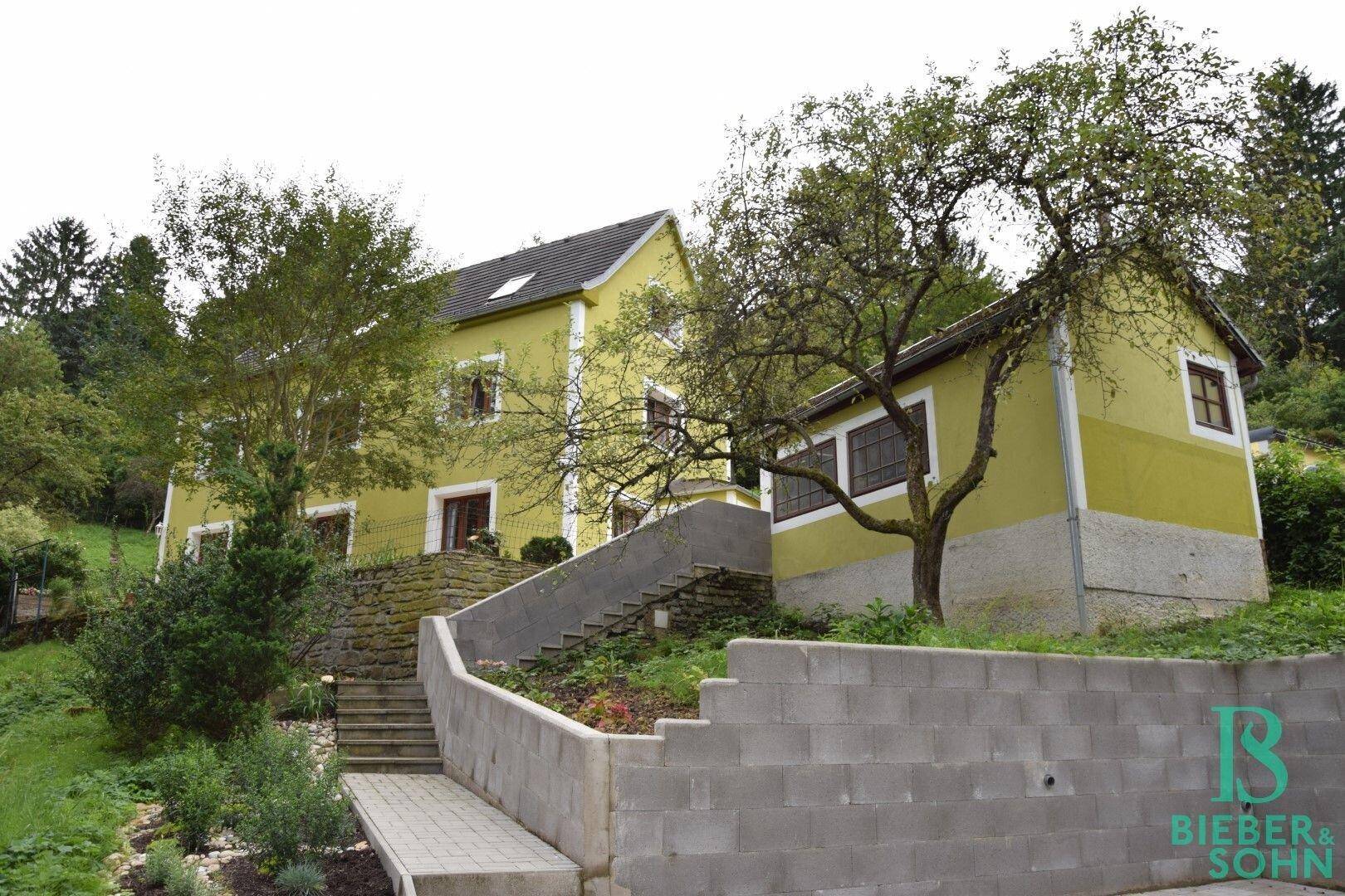 Ansicht des Hauses in Hanglage mit mehreren Gebäudeteilen und viel Grün.