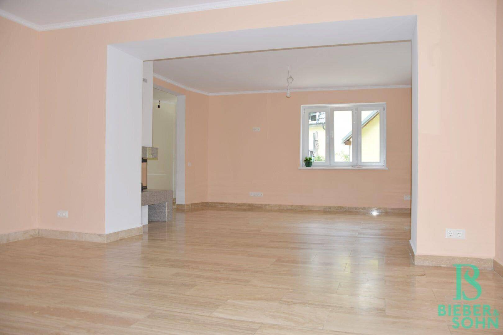Helles Wohnzimmer mit großen Fenstern, Fliesenboden und Blick ins Grüne.