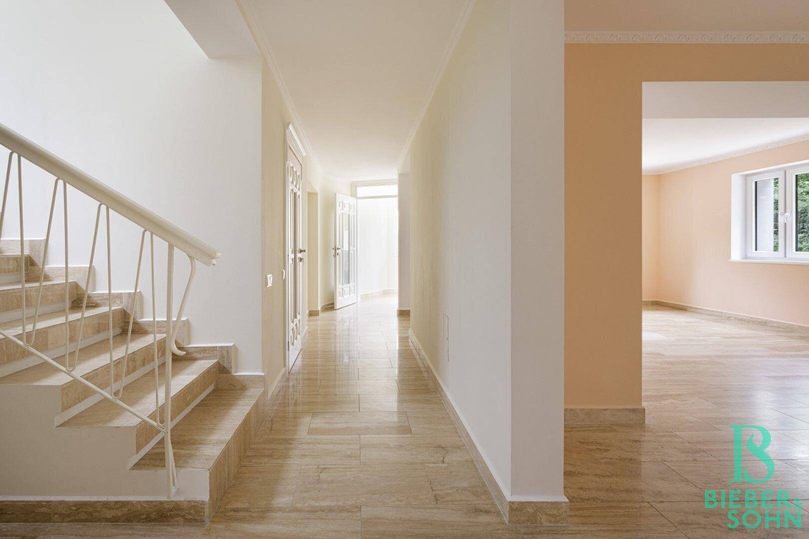 Heller Flur mit Fliesenboden, Treppe und mehreren Türen zu angrenzenden Zimmern.