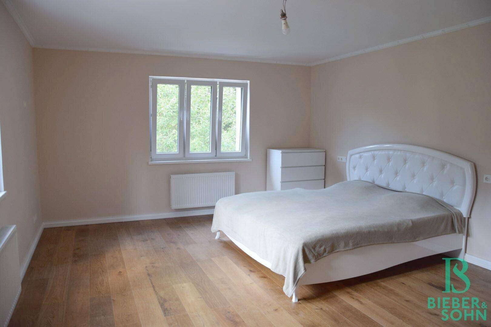 Gemütliches Schlafzimmer mit Holzfußboden, großem Fenster und Blick ins Grüne.