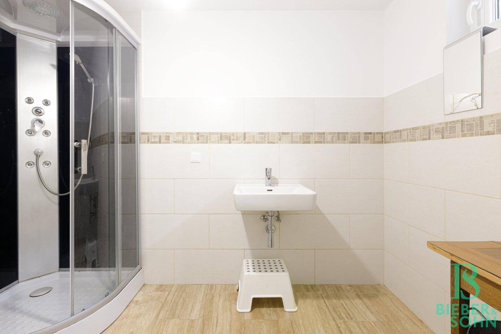 Modernes Badezimmer mit Duschkabine, Waschbecken und hellen Fliesen.