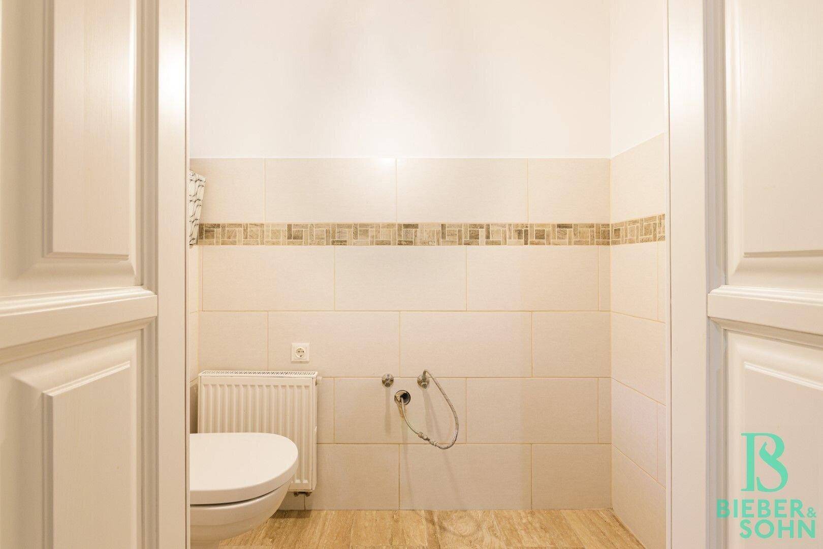 Separates WC mit Wand-WC und hellen Fliesen an den Wänden.